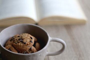 Bowl of chocolate chip cookies and open book on a table. Selective focus.