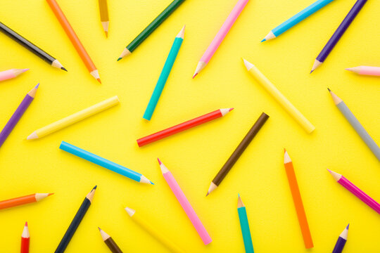 Many new colorful pencils on bright yellow table. Pattern background. Closeup. Top down view.