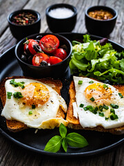 Continental breakfast - sunny side up eggs on toasted bread with fresh vegetable salad on wooden table