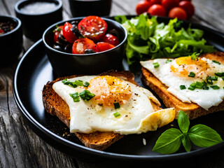 Continental breakfast - sunny side up eggs on toasted bread with fresh vegetable salad on wooden table