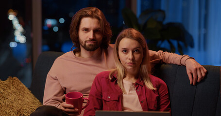 Portrait of cheerful man and woman holding coffee cup using laptop posing positive at camera. Living room, style apartment. Relationships.