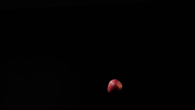 Flying red apple, close up at ripe red apple flies up and spinning on a black background in slow motion shot, vivid fruit display