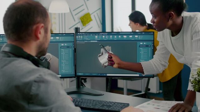 Black employee pointing on monitor explaining to project manager mechanical metalic parts of motor prototype. Industrial engineers using 3D cad program with gears shape working in creative office