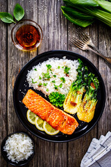 Fried salmon steak with lemon, jasmine rice and fried pak choi cabbage served on wooden table
