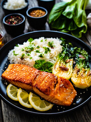 Fried salmon steak with lemon, jasmine rice and fried pak choi cabbage served on wooden table
