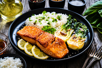 Fried salmon steak with lemon, jasmine rice and fried pak choi cabbage served on wooden table
