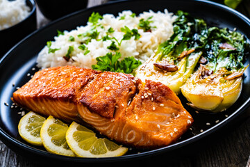 Fried salmon steak with lemon, jasmine rice and fried pak choi cabbage served on wooden table
