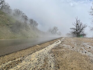 Close up of wet road in fog in mountainous terrain. Asphalt road after rain in foggy and cloudy weather.