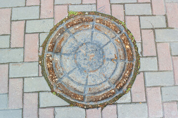 Old iron shabby sewer hatch embedded in the paving stones