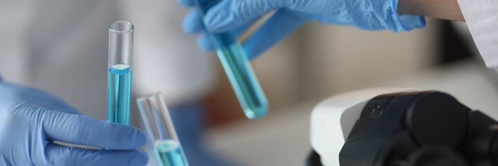 Hands in protective rubber gloves holding in test tube with blue liquid in laboratory