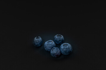 ein paar dunkle, frische Blaubeeren auf schwarzem, dunklen Hintergrund. Minimalistisch im Querformat mit viel Platz für Text , sehr geringe Schärfentiefe