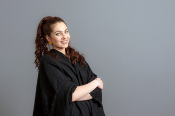 portrait of charming curly-haired woman in a black cloak isolated on a gray background