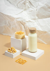 Fototapeta na wymiar Vegetable pea milk in a bottle and chickpeas in bowl on white podium,pedestal on beige crumpled paper background. shadows. lactose free vegan product.Modern composition.Isometric diagonal projection