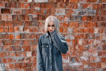 Portrait of young blonde girl on background of red b rick wall.