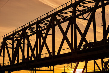 The silhouette of the metal structure of the railway bridge at sunset. Engineering structure made of steel against the sky.