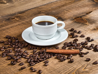 Cup of freshly brewed coffee with scattered coffee beans and cinnamon