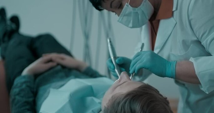 The female dentist is taking from the dental holder the dental drill for use in the dental treatment of a male patient.