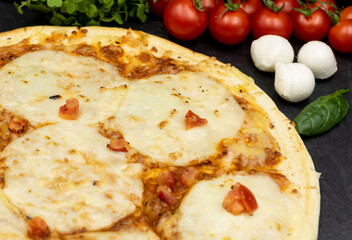 Pizza with mozzarella on a black background close-up with ingredients.