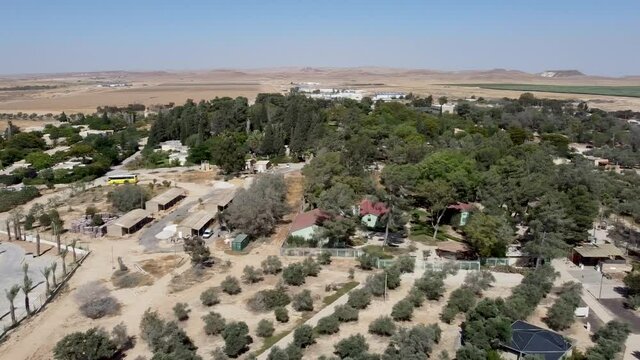 Aerial slide to the right  drone shot of a panoramic view of kibbutz Sde-Boker and the area around it, filled with trees, bushes, fields, trails, buildings and houses. Blue sky, Day.