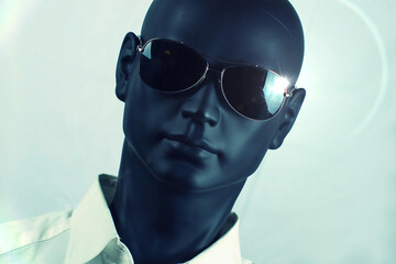 Dark plastic mannequin head with sunglasses and white shirt, light reflections and greenish color dominance.