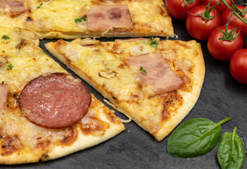 Pizza with ham, salami and mushrooms on a black background close-up with ingredients.