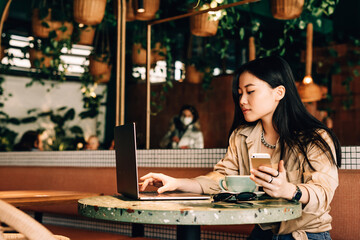 Asian girl working at a laptop, drinking coffee and using the phone in a cafe, business woman