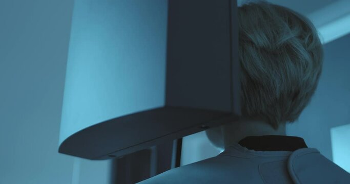 Close-up back view a woman patient who is standing in the 3D dental tomography scan which is rotating around of her head and providing a full mouth x-ray.