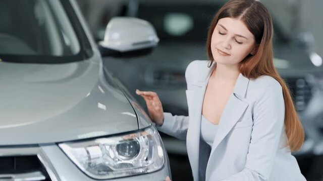 Stylish girl sitting near a new car kisses the bumper and hugs