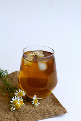 chamomile tea on sackcloth. glass cup of iced Herbal chamomile tea on a white table with copy space. cup of tea with fresh flowers and green leaves on white background. vertical
