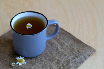 hot drinks. grey mug of chamomile tea on sackcloth. cup of hot Herbal chamomile tea on a wooden table with copy space with fresh flowers and green leaves on light background.