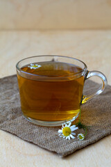 cup of tea.glass cup of hot Herbal chamomile tea on a wooden table with copy space with fresh flowers and green leaves on light background. hot drinks. mug of chamomile tea on sackcloth. vertical
