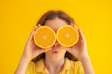 Child holding orange halves instead of sunglasses