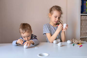 Brother and sister are preparing for Easter. Children's draw on decorative eggs. Home classes for children.Children's emotions.Children draw with felt-tip pens on decorative eggs