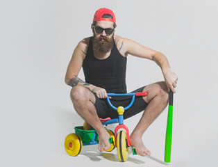 Man on a childrens bicycle. Bicycle rider, bearded angry man holds green baseball bat on bicycle...