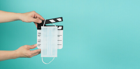 Fack mask on clapperboard and hand is holding clapper board or movie slate.It is used in film production and movies industry on green mint or Tiffany Blue background.