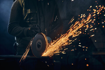 Close up of man in special dark suit and black protective gloves working angle grinder for metal...