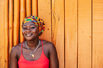 African woman with a hopeful happy smile standing against a painted wooden wall in the tropical...