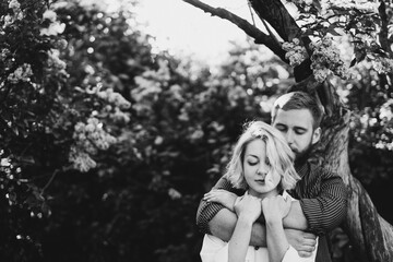 Romantic and happy caucasian couple in casual clothes hugging on the background of beautiful blooming lilac. Love, relationships, romance, happiness concept. Man and woman walking outdoors together.