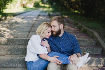 Fototapeta premium Romantic and happy caucasian couple in casual clothes hugging on the background of beautiful blooming lilac. Love, relationships, romance, happiness concept. Man and woman walking outdoors together.