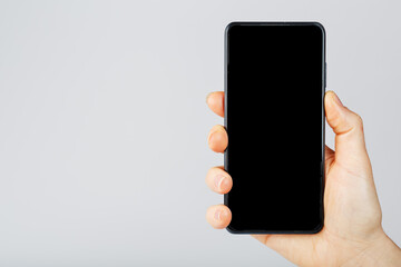 The hand holds a black smartphone with a blank black screen and a modern frameless design