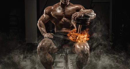 Foto op Plexiglas Muscular man sits on a bench with dumbbells burning. Bodybuilding and powerlifting concept. © andy_gin