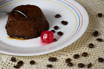 Spoon plunged into a Tasty Coffee Flan on a plate decorated with a cherry and coffee beans