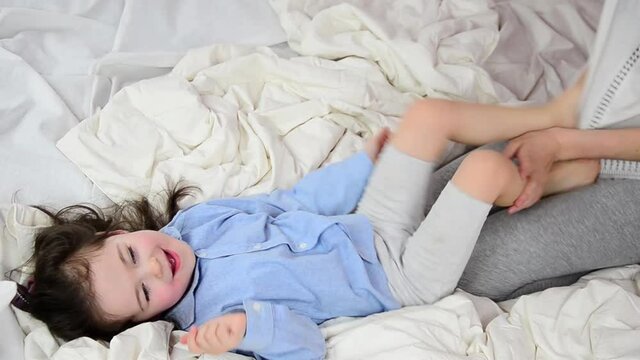 Happy mother and little daughter are playing on the bed. Happy child plays with his mother. Children's emotions. A happy family. A trusting relationship between mother and daughter