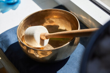The mallet from a singing bowl lies in the singing bowl. It is on blue background and stands on a...