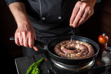 The chef adds salt to pan with raw meat sausage. Preparation for cooking sausages in the kitchen of a restaurant or cafe on table with vegetables