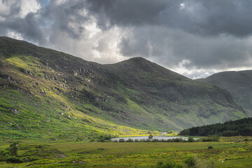Fototapeta premium Small lake, Lough Gummeenduff in Black Valley, rocky hills of MacGillycuddys Reeks mountains illuminated by sunlight, Ring of Kerry, Ireland