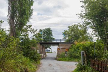 Beautiful landscape view. Small road passing under bridge. Green trees on cloudy sky background. Sweden.