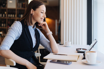 Attractive female with cute smile having a coffee while reading on tablet relaxing in a break