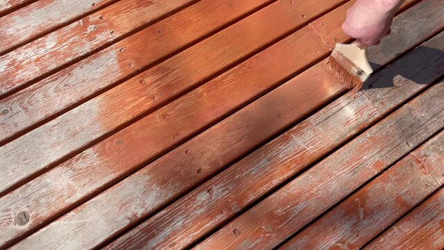 Male hand brushing new stain on home outdoor cedar wooden deck boards 
