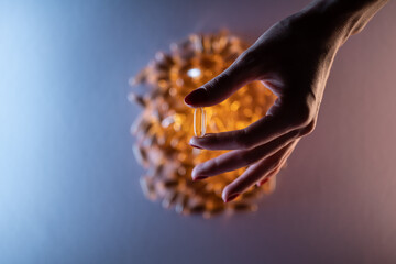 close up of hand holding fish oil capsule or omega 3 vitamins on blue background